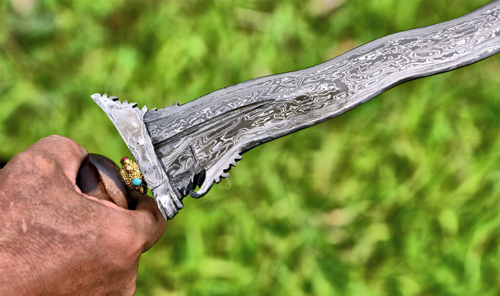  A hand holding a traditional wavy-bladed Indonesian keris dagger with a golden handle against a blurred background of foliage.